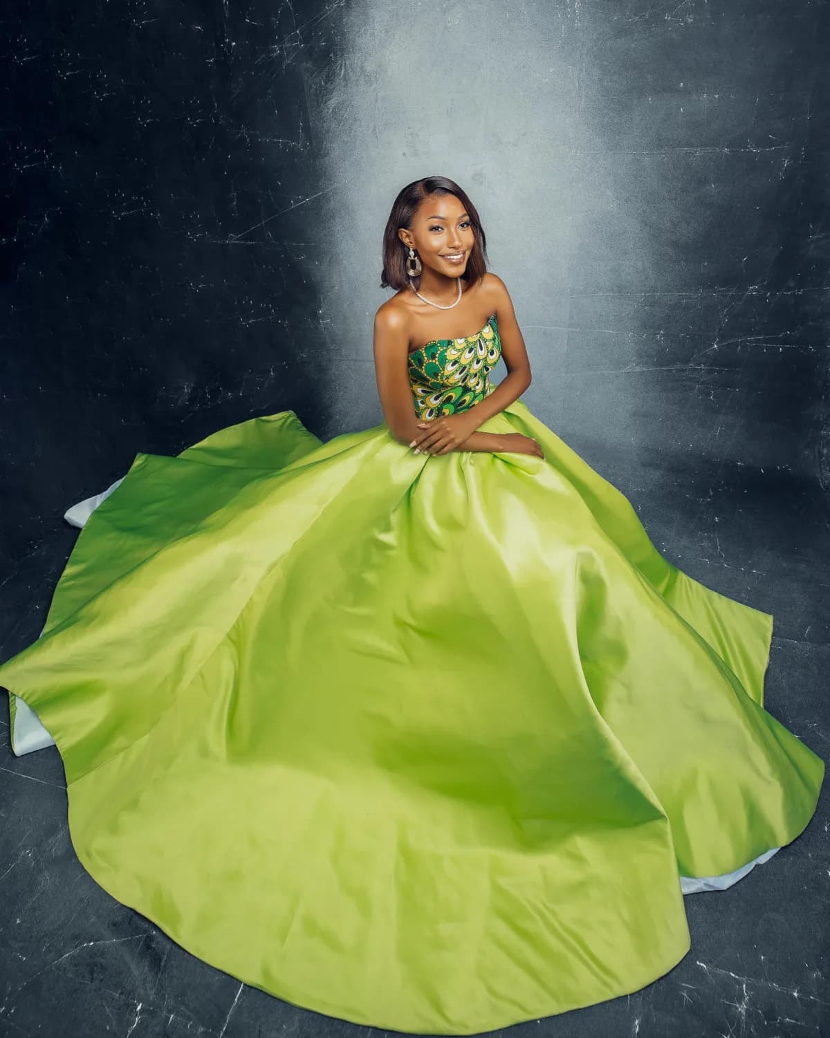 A young Tanzanian woman seated in a green kitenge and satin ball gown